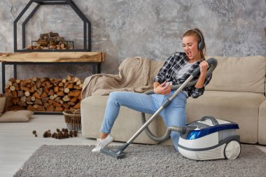 Tam uzunlukta portre neşeli genç kadının 20'li yaşlarda kulaklık ile müzik dinlemek ve evde elektrikli süpürge ile eğleniyor.
