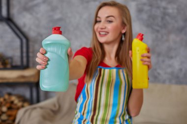 Kadın karşılaştırır iki deterjan şişesi evde oturma odasında temizlik. Ev iş.