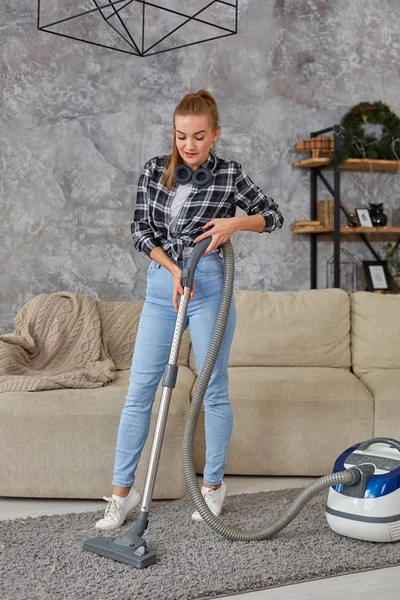 Joven mujer sonriente aspiradora limpiando la alfombra en la sala de estar, interior escandinavo moderno. Hogar, concepto de limpieza — Foto de Stock