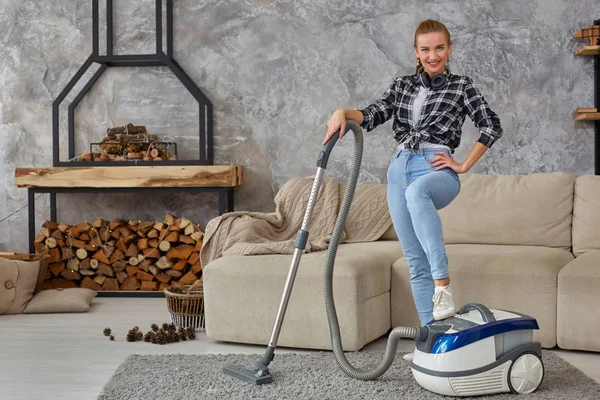 Joven mujer sonriente aspiradora limpiando la alfombra en la sala de estar, interior escandinavo moderno. Hogar, concepto de limpieza — Foto de Stock