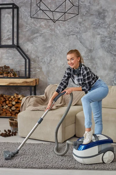 Joven mujer sonriente aspiradora limpiando la alfombra en la sala de estar, interior escandinavo moderno. Hogar, concepto de limpieza — Foto de Stock