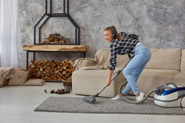 Portrait complet d'une jeune femme joyeuse de 20 ans écoutant de la musique via un casque et s'amusant avec un aspirateur dans la maison . — Photo