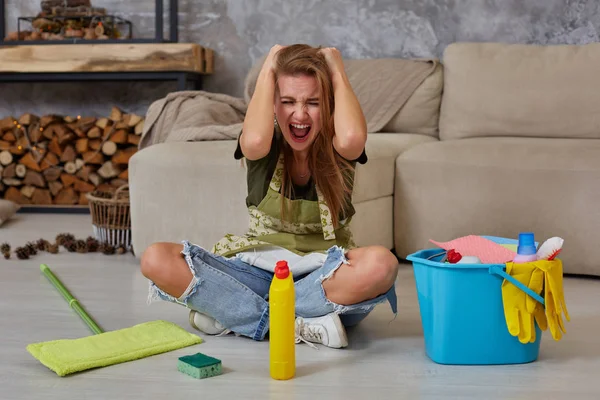 Frustrierte junge Frau sitzt mit Putzutensilien und Ausrüstung auf dem Wohnzimmerboden und schreit — Stockfoto