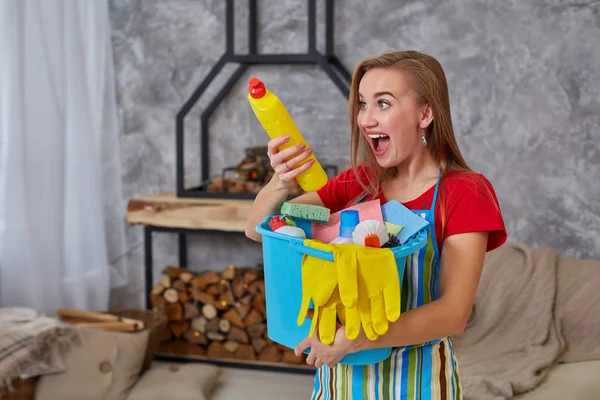 Detergente close-up para limpeza em mãos de mulher emocional ou dona de casa com muitos objetos domésticos em balde azul na sala de estar . — Fotografia de Stock