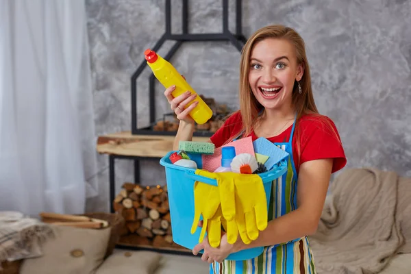 Nahwaschmittel zur Reinigung emotionaler Frauen- oder Hausfrauenhände mit vielen Haushaltsgegenständen im blauen Eimer im Wohnzimmer. — Stockfoto