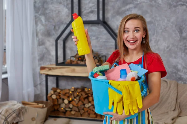 Nahwaschmittel zur Reinigung emotionaler Frauen- oder Hausfrauenhände mit vielen Haushaltsgegenständen im blauen Eimer im Wohnzimmer. — Stockfoto