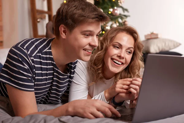 Gülümseyen genç çift erkek ve kadın yatakta yatan ve laptop bir şey izliyor