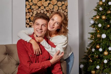 Mutlu genç güzel çift salon Sunni Noel ağacı yakınındaki kanepede oturan üzerinde