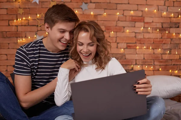 Sorrindo jovem casal homem e mulher sentados na cama e usando seu laptop — Fotografia de Stock