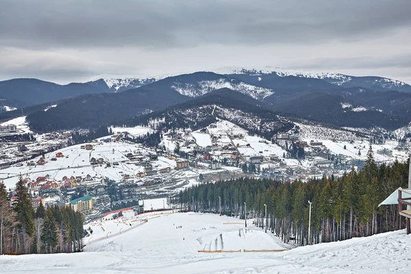 Panorama von Skigebiet, Piste, Menschen am Skilift, Skifahrer auf der Piste zwischen grünen Kiefern und Schneelanzen. — Stockfoto