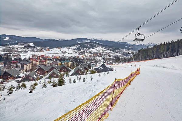 Panorama von Skigebiet, Piste, Menschen am Skilift, Skifahrer auf der Piste zwischen grünen Kiefern und Schneelanzen. — Stockfoto