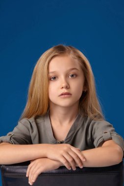 Gri gözleri ve sarı saçlı küçük kız bir sandalyede oturur