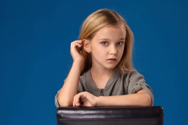 Gri gözleri ve sarı saçlı küçük kız bir sandalyede oturur