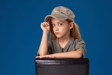 Gri gözleri ve sarı saçlı bir sandalyede oturan şapkalı küçük kız