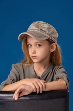 Gri gözleri ve sarı saçlı bir sandalyede oturan şapkalı küçük kız