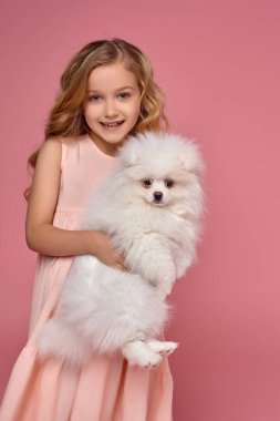 Pembe elbiseli sarışın bir kıvırcık saçlı küçük kız köpeğiyle oynuyor