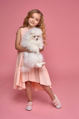 Pembe elbiseli sarışın bir kıvırcık saçlı küçük kız köpeğiyle oynuyor