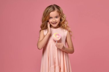 Pembe elbiseli sarışın bir kıvırcık saçlı küçük kız bir şeker ile poz