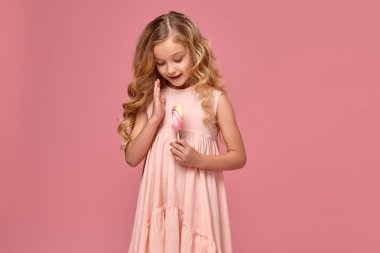 Pembe elbiseli sarışın bir kıvırcık saçlı küçük kız bir şeker ile poz