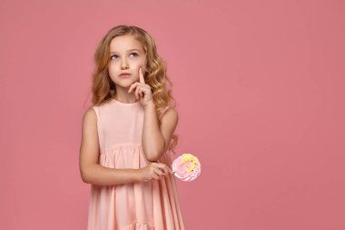 Pembe elbiseli sarışın bir kıvırcık saçlı küçük kız bir şeker ile poz