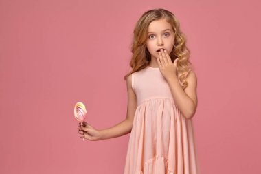 Pembe elbiseli sarışın bir kıvırcık saçlı küçük kız bir şeker ile poz