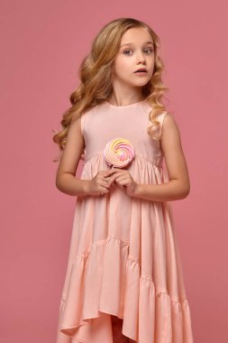 Pembe elbiseli sarışın bir kıvırcık saçlı küçük kız bir şeker ile poz