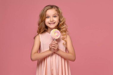 Pembe elbiseli sarışın bir kıvırcık saçlı küçük kız bir şeker ile poz