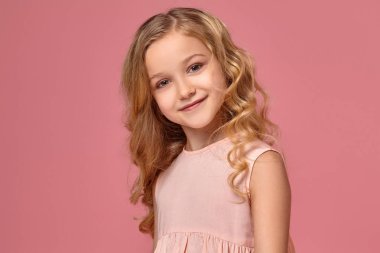 Pembe elbiseli sarışın bir kıvırcık saçlı küçük kız kamera için poz