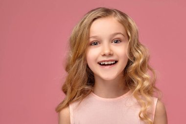 Pembe elbiseli sarışın bir kıvırcık saçlı küçük kız kamera için poz