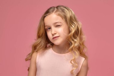 Pembe elbiseli sarışın bir kıvırcık saçlı küçük kız kamera için poz