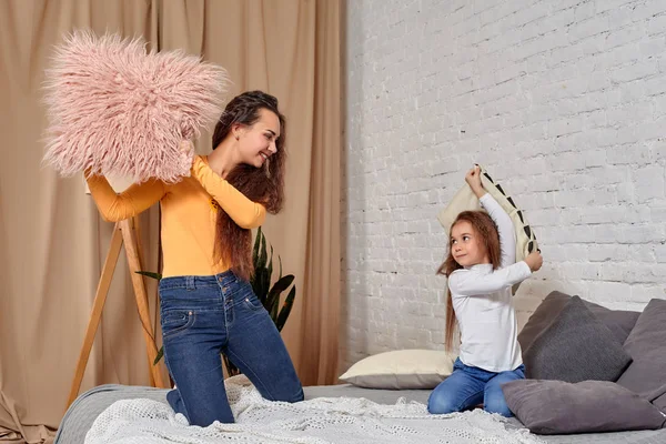 Genç anne ve kızı yatakta yastık savaşı ile eğlenmeyi — Stok fotoğraf
