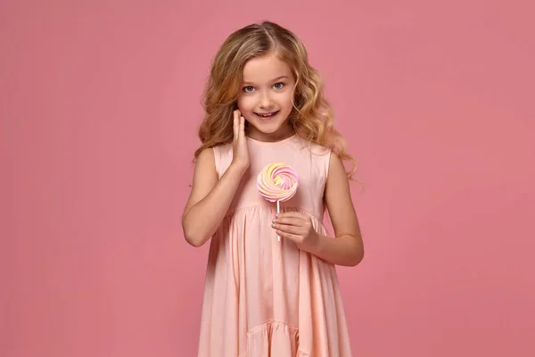 Egy szőke göndör haja, egy rózsaszín ruhás kislány jelentenek azokkal a candy — Stock Fotó