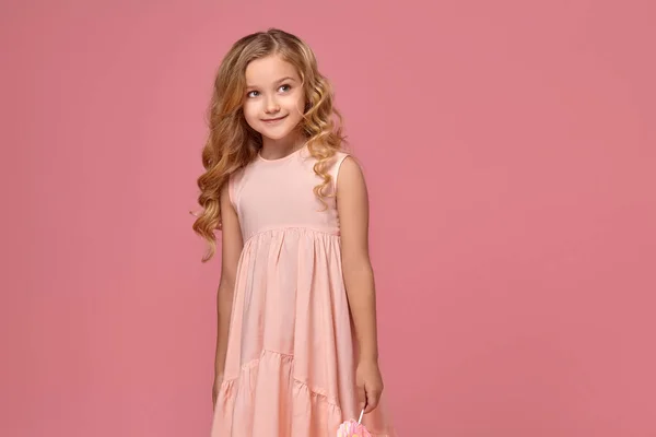 Niña con el pelo rubio rizado, en un vestido rosa está posando con un caramelo —  Fotos de Stock