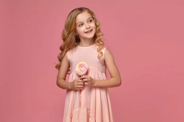 Egy szőke göndör haja, egy rózsaszín ruhás kislány jelentenek azokkal a candy — Stock Fotó