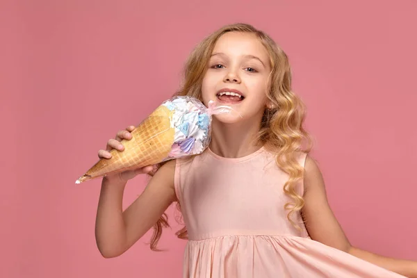 Menina com um cabelo encaracolado loiro, em um vestido rosa está posando com um sorvete — Fotografia de Stock