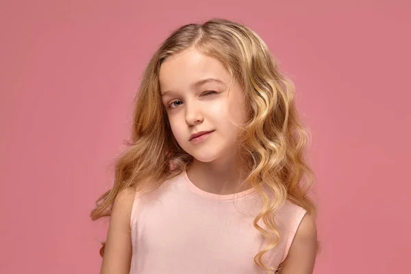 Malá dívka s kudrnatými blond vlasy, v růžových šatech pózuje pro kamery — Stock fotografie