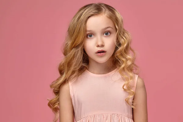 Egy szőke göndör haja, egy rózsaszín ruhás kislány pózol a kamera — Stock Fotó