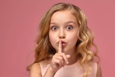 Pembe elbiseli sarışın bir kıvırcık saçlı küçük kız kamera için poz