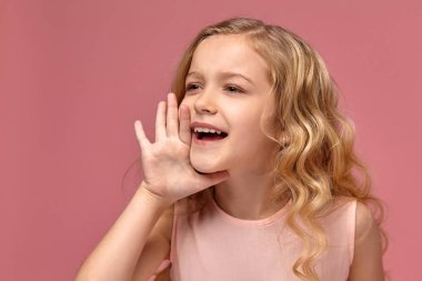 Pembe elbiseli sarışın bir kıvırcık saçlı küçük kız kamera için poz