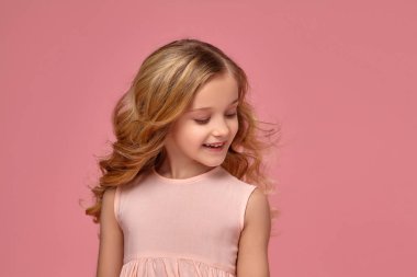 Pembe elbiseli sarışın bir kıvırcık saçlı küçük kız kamera için poz
