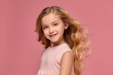 Pembe elbiseli sarışın bir kıvırcık saçlı küçük kız kamera için poz