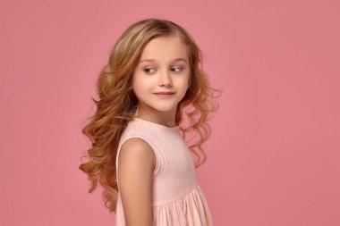 Pembe elbiseli sarışın bir kıvırcık saçlı küçük kız kamera için poz