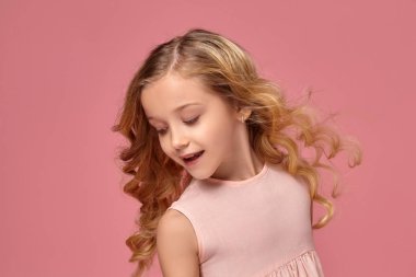 Pembe elbiseli sarışın bir kıvırcık saçlı küçük kız kamera için poz