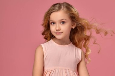 Pembe elbiseli sarışın bir kıvırcık saçlı küçük kız kamera için poz