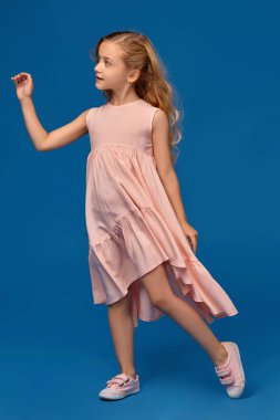 Pembe elbiseli şık küçük kız mavi bir arka plan üzerinde poz.