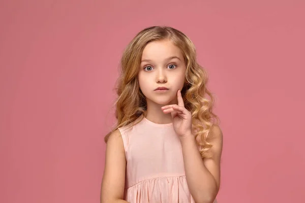 Egy szőke göndör haja, egy rózsaszín ruhás kislány pózol a kamera — Stock Fotó