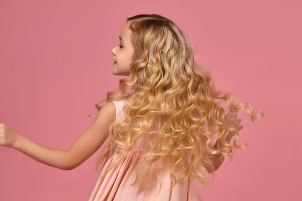 Menina com um cabelo encaracolado loiro, em um vestido rosa está posando para a câmera — Fotografia de Stock
