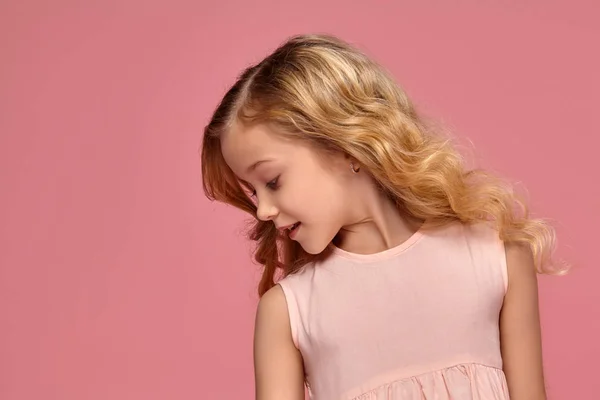 Kleines Mädchen mit blonden lockigen Haaren posiert in einem rosa Kleid für die Kamera — Stockfoto