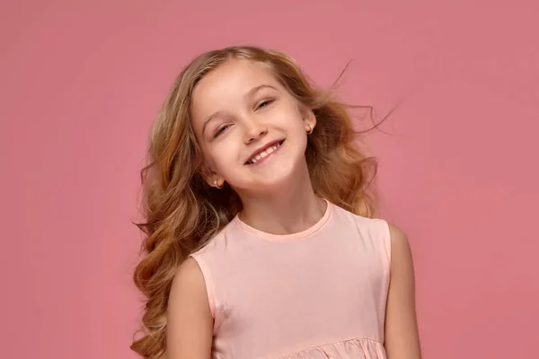 Niña con el pelo rubio rizado, en un vestido rosa está posando para la cámara — Foto de Stock