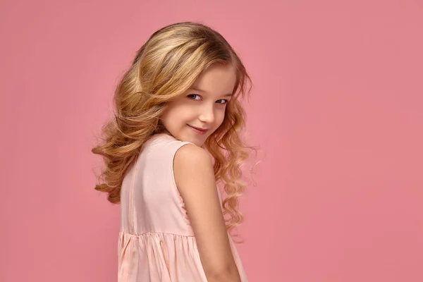 Niña con el pelo rubio rizado, en un vestido rosa está posando para la cámara —  Fotos de Stock